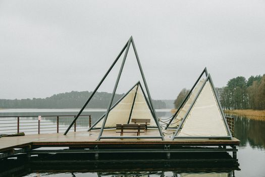 Unique triangular tents sit on a wooden pier overlooking a serene lake in Poland. Perfect for outdoor exploration.