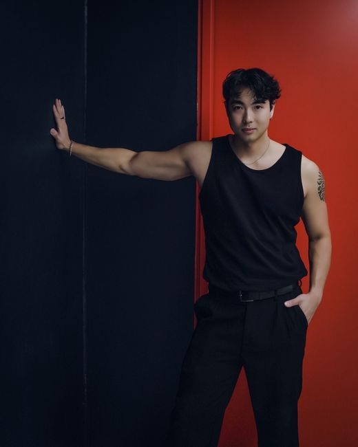 Stylish young man posing confidently in black attire against a striking red wall.