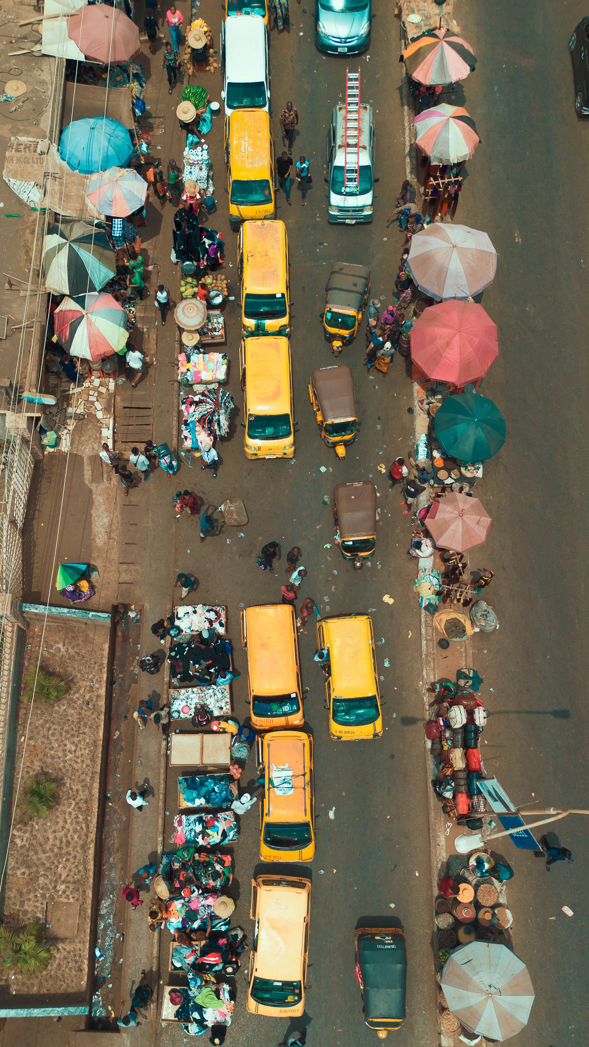Colorful market street bustling with yellow buses and vendors in Enugu, Nigeria.