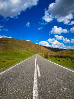 Empty road stretching through green hills under a vibrant blue sky with clouds.