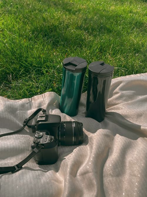 Free A DSLR camera and two coffee mugs on a blanket outdoors in green grass. Stock Photo
