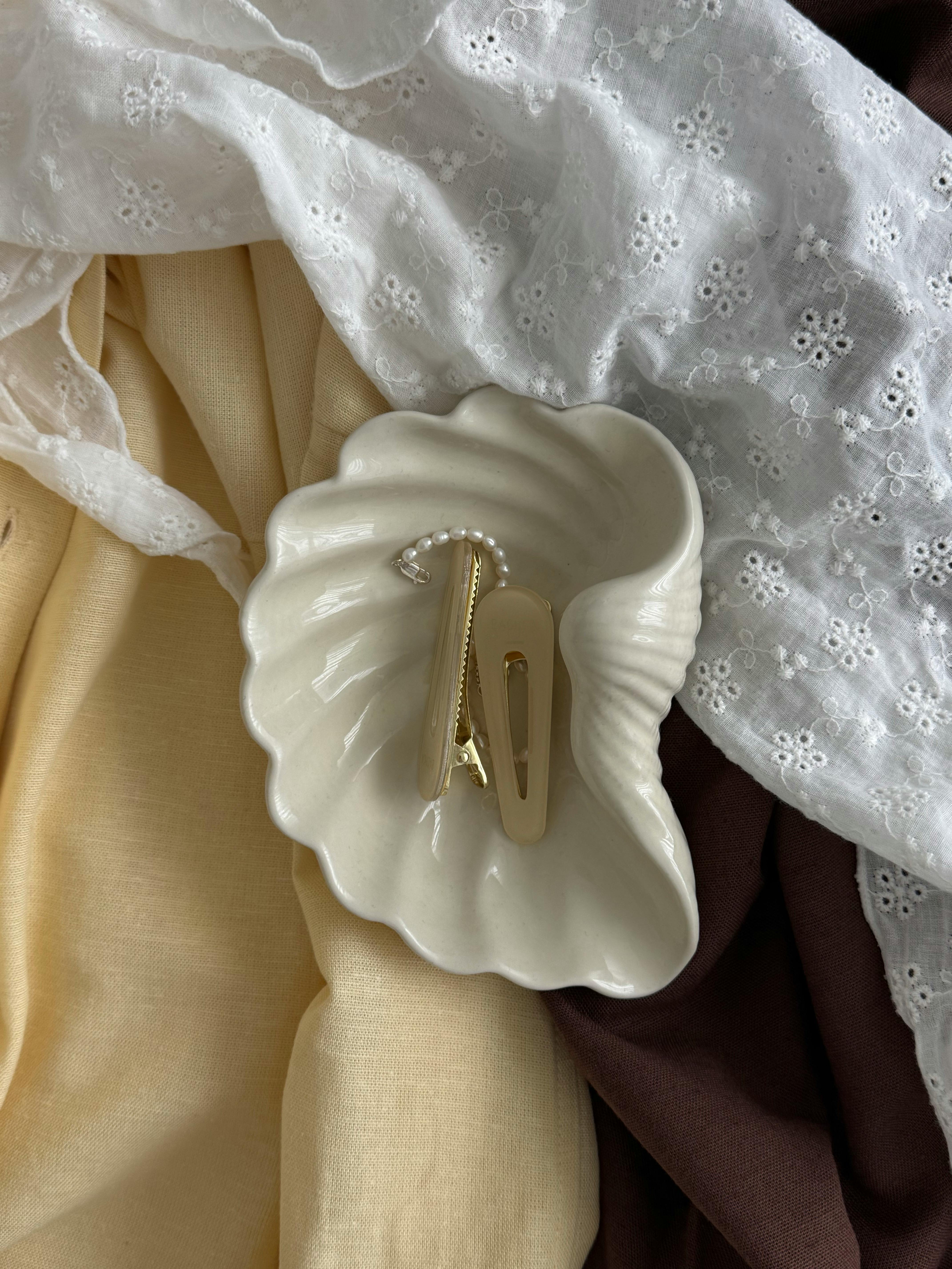 Aesthetic arrangement of hair clips in a shell dish on textured fabrics, exuding elegance.