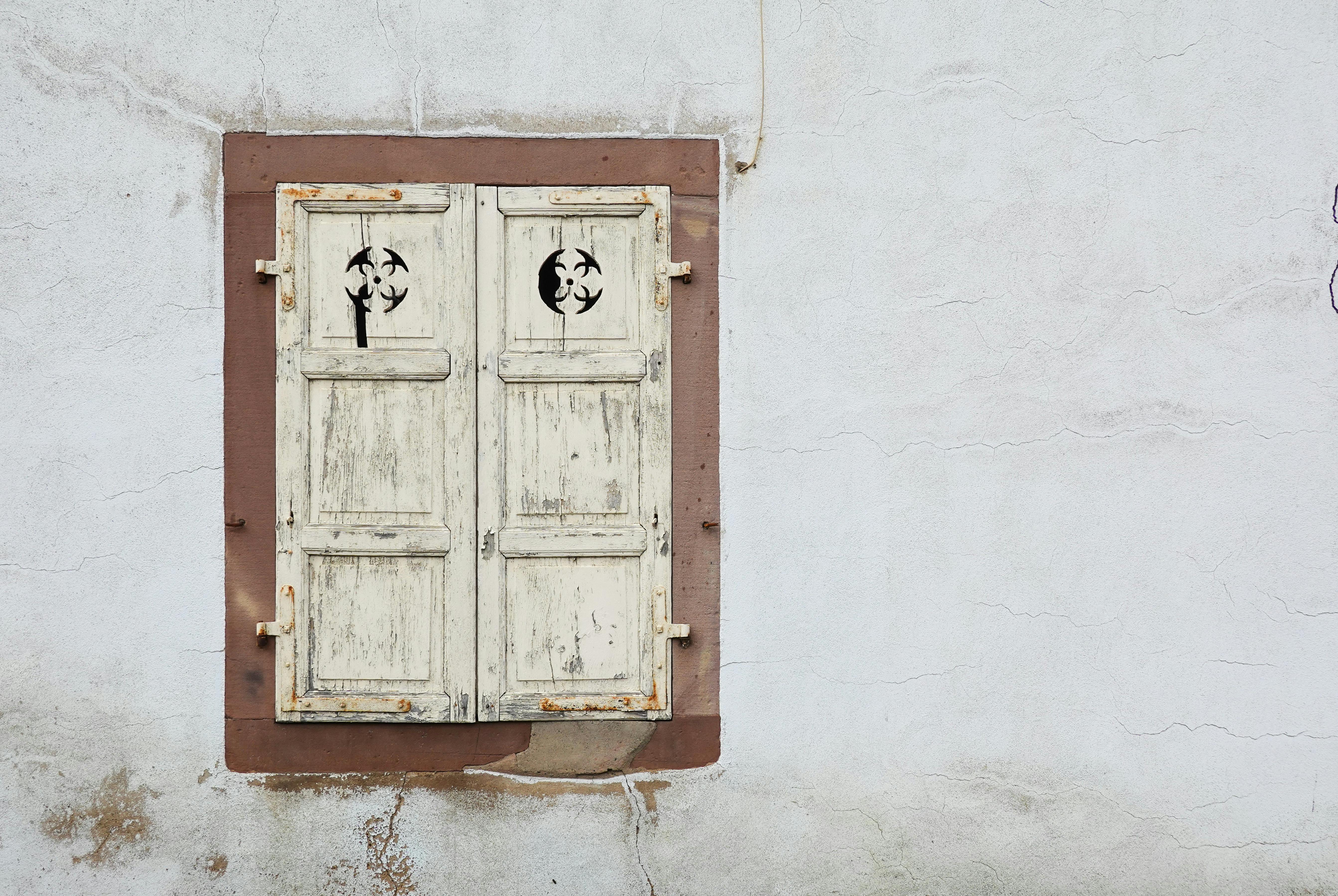 Rustic, decorative wooden shutter on an old, textured wall, showcasing vintage charm.