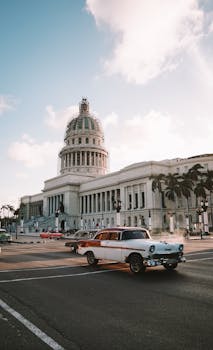 Vintage car driving past El Capitolio in Havana, showcasing Cuban architecture.