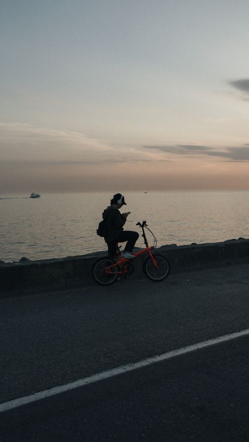 Free A cyclist pauses on a seaside road at twilight, enjoying the calm sunset by the ocean. Stock Photo