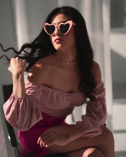 Free Fashionable woman with heart sunglasses enjoying the sunlight indoors. Chic and trendy vibes. Stock Photo