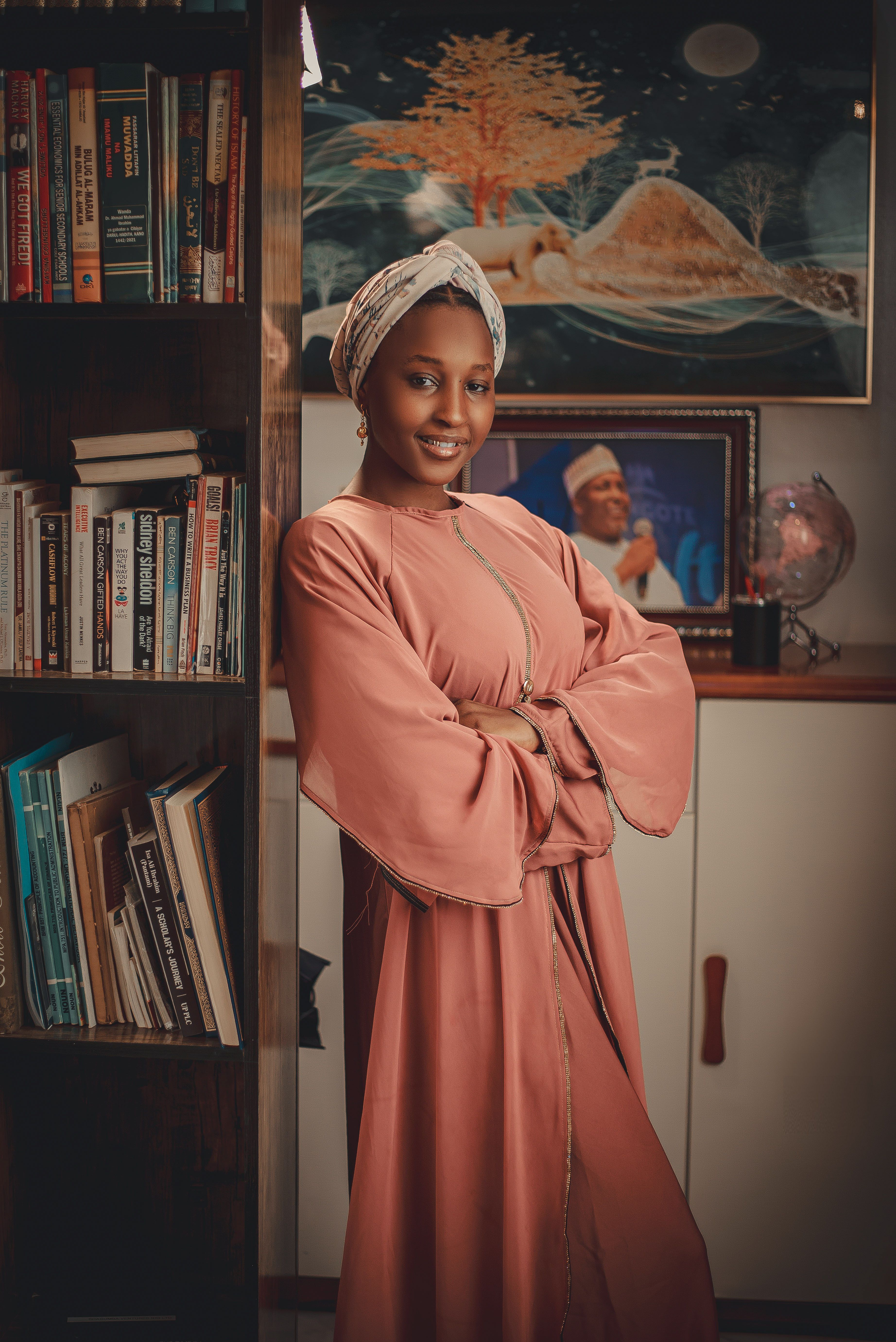 Smiling woman in traditional attire posing by a bookshelf indoors.