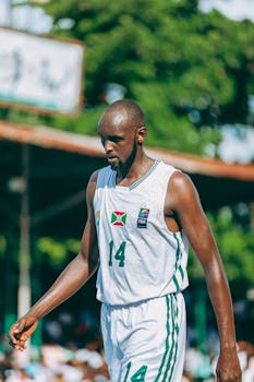 A tall basketball player focuses during an outdoor tournament under the bright sun.