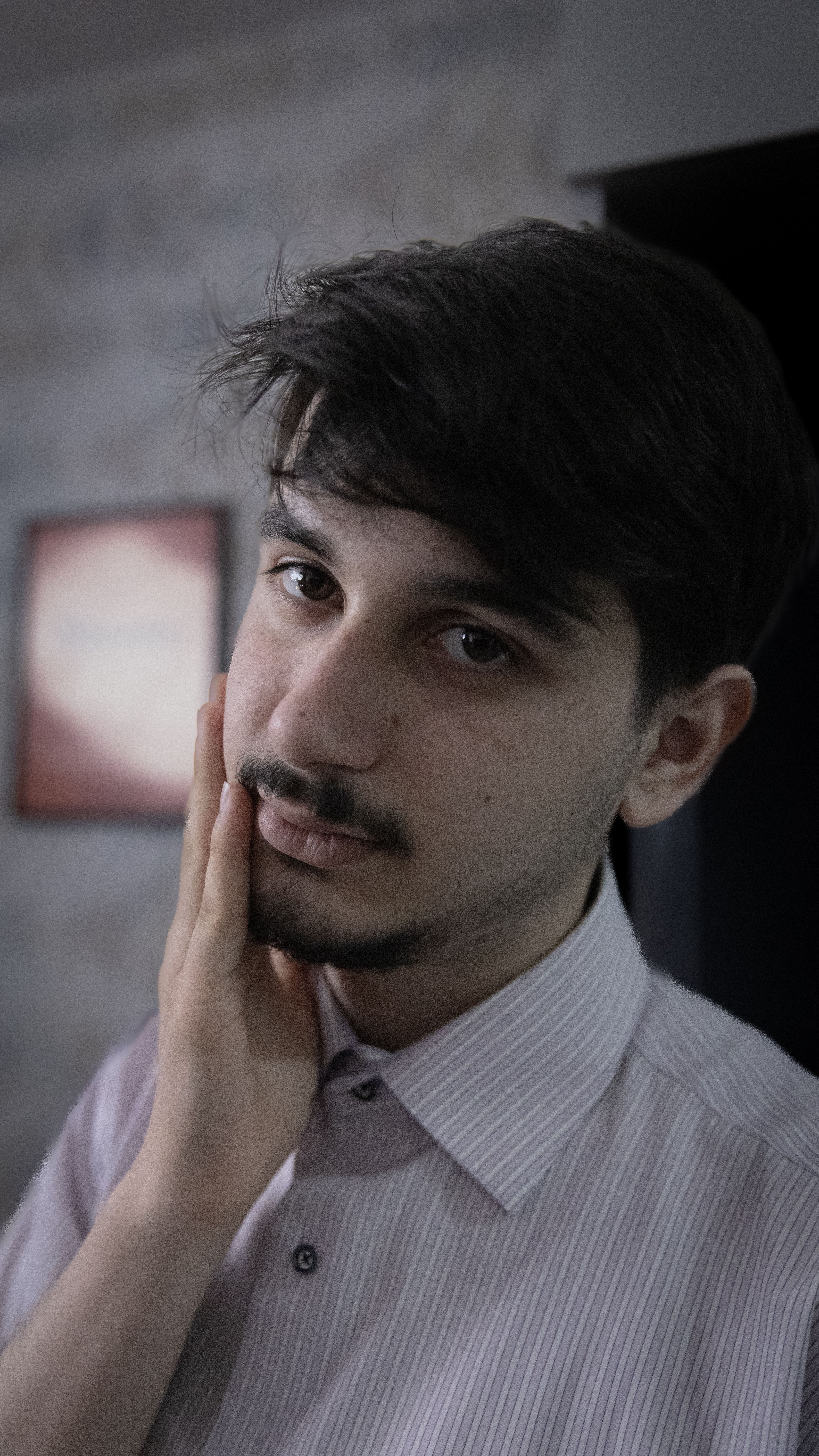 Thoughtful young man indoors, gently touching his face with natural light.