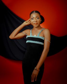 Chic portrait of a woman in a black dress with a red and black backdrop, exuding elegance.