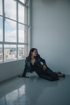 Stylish woman in a leather jacket sitting by a window in a modern loft with city views.