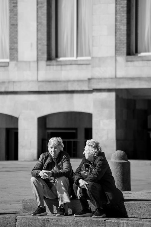 Free Two senior adults engaged in conversation on city steps, captured in black and white. Stock Photo