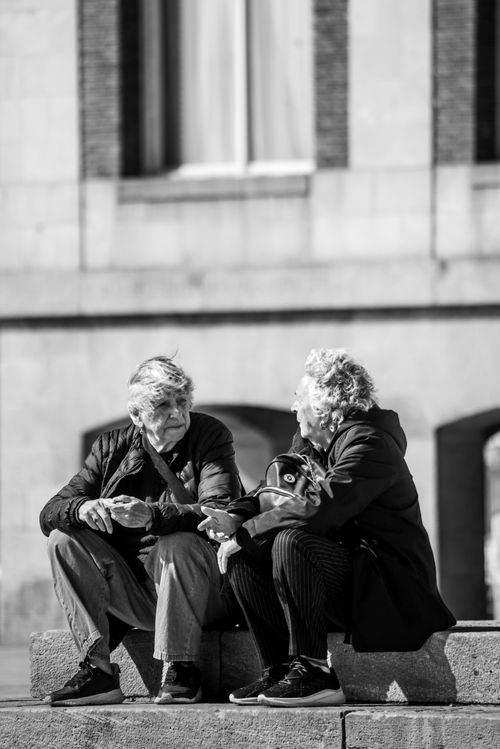 Free Two seniors chatting on a city bench in black and white, urban setting. Stock Photo