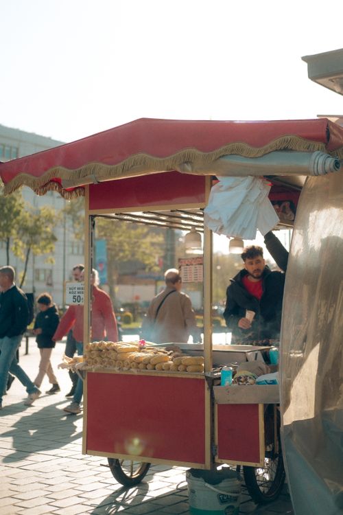 Free Red cart with street vendor selling fresh pastries in a bustling outdoor city setting. Stock Photo