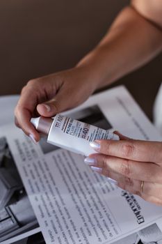 Close-up of hands holding sunscreen SPF 40 tube above a magazine page indoors.