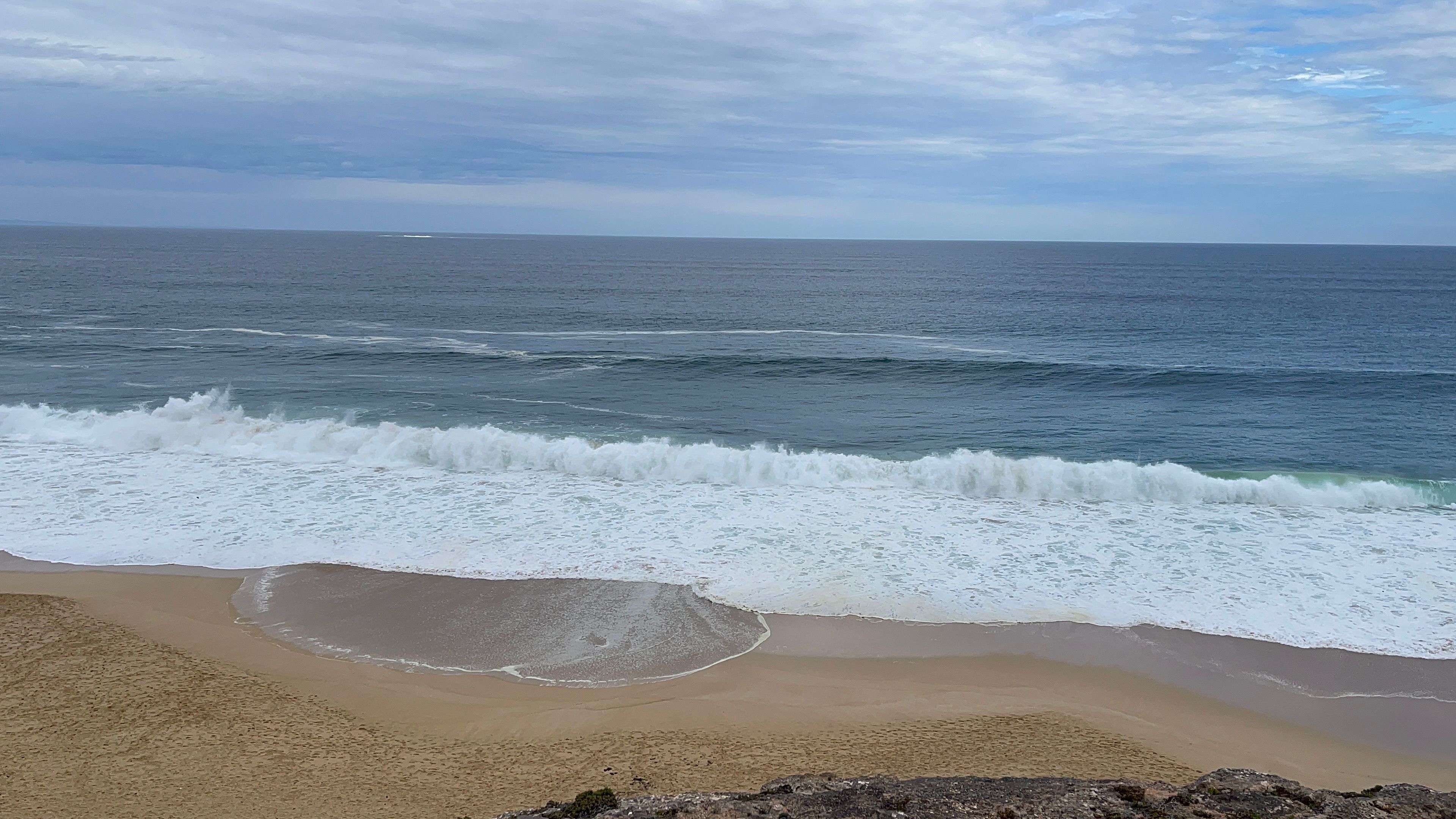 Empty white sand and breaking surf on Long Beach at Kommetjie with Slangkop lighthouse behind