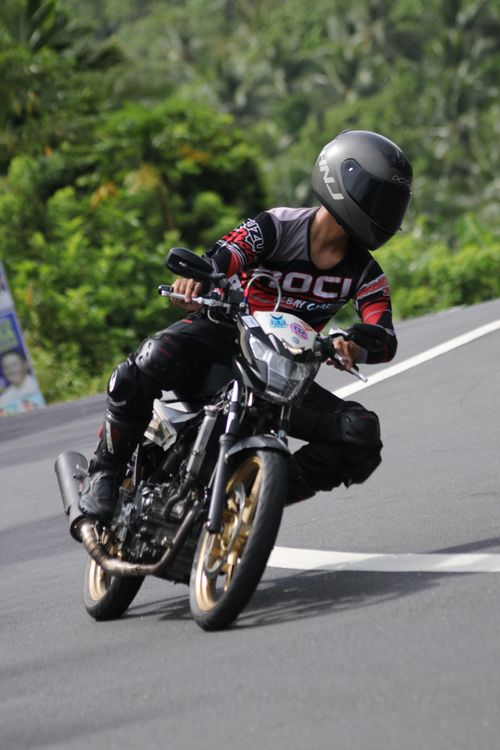 Free A motorcyclist speeds and leans into a sharp curve on a forested road. Stock Photo
