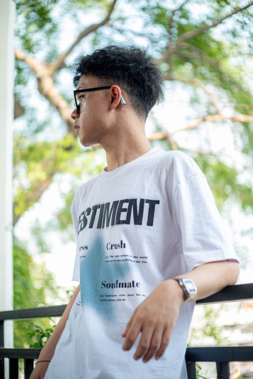 Free Fashionable young man wearing a graphic tee and AirPods, standing outdoors with a stylish look. Stock Photo