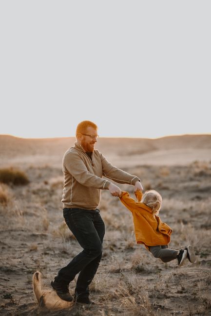 Heartwarming image of a father swinging his child playfully at sunset in a desert landscape.
