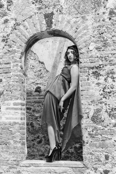 Black and white portrait of an elegant model in a flowing dress posing in a historic stone archway in Mexico City.