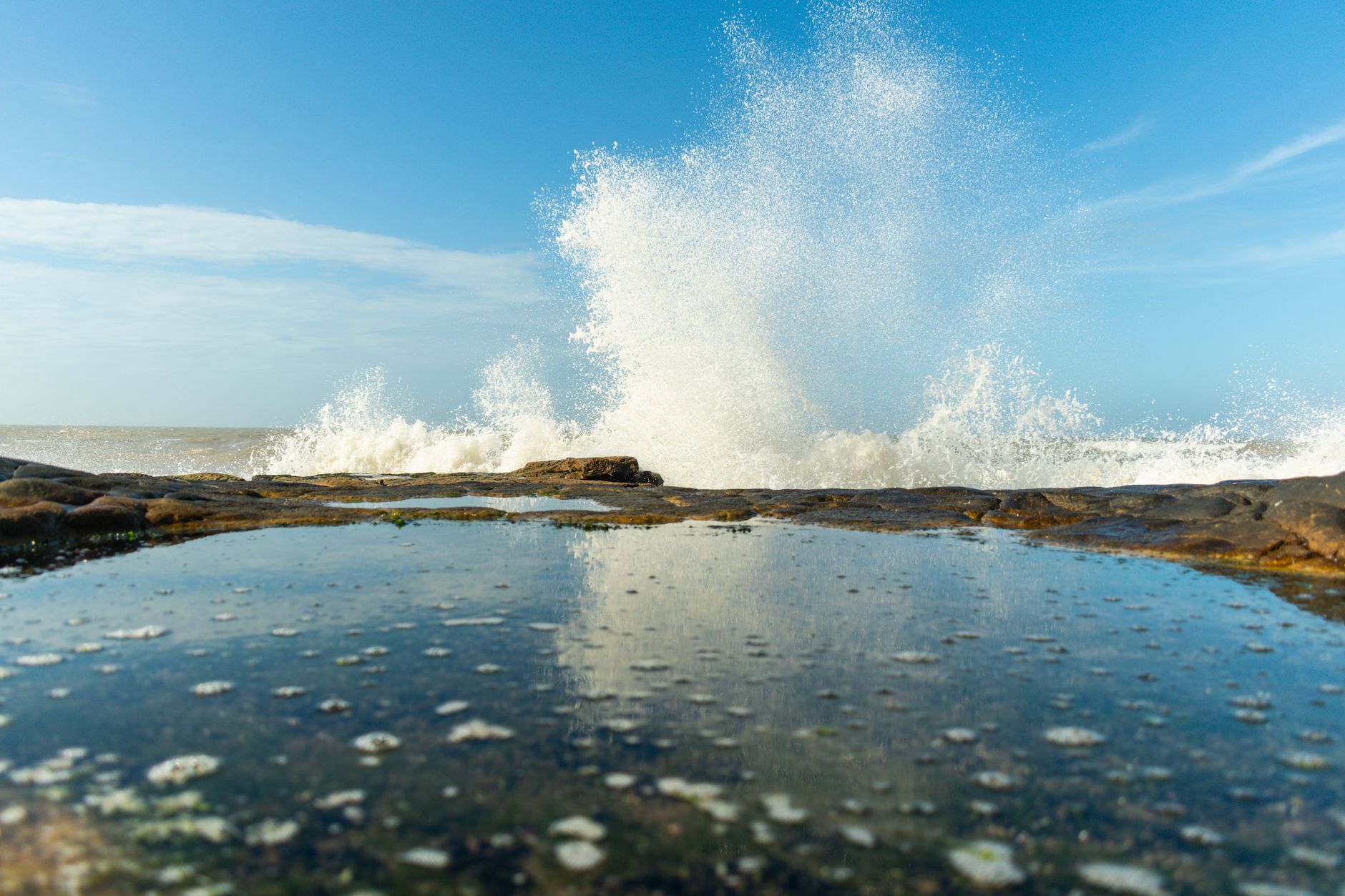 A vivid capture of ocean waves crashing against rocks under a clear blue sky in Mar del Plata, Argentina.