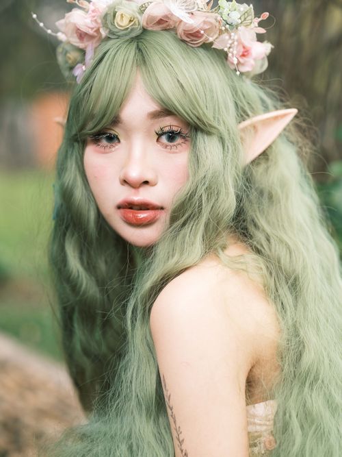 Free Enchanting portrait of a woman in elf cosplay with green hair and floral crown outdoors. Stock Photo