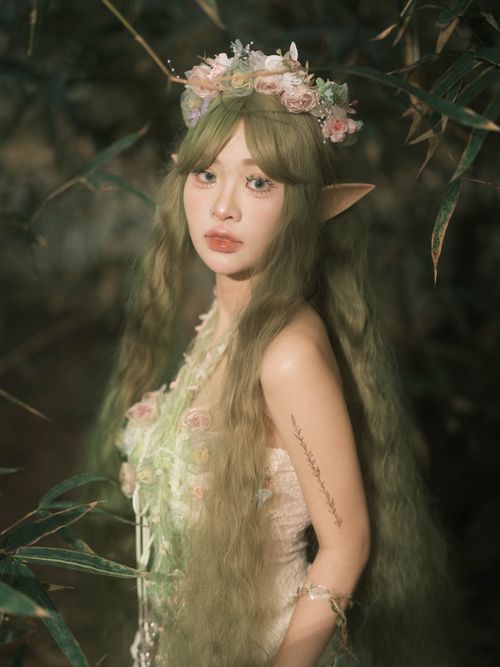 Free A mystical female elf with green hair and floral crown in a serene forest setting. Stock Photo