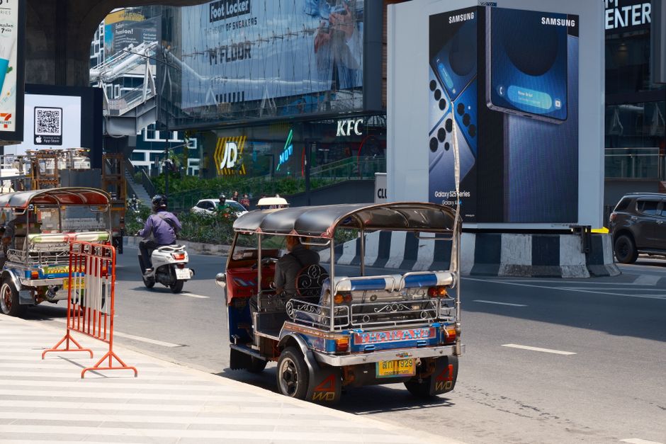 A lively street scene in Bangkok featuring tuk-tuks and motorbikes under a clear sky.
