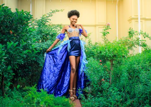 A striking model poses in a vibrant dress amidst lush greenery, exuding elegance and style.