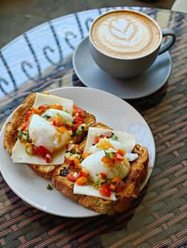 Delicious breakfast toast topped with poached eggs and fresh veggies beside a latte.