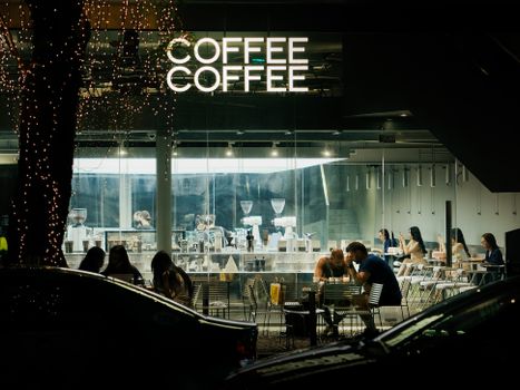 Cozy coffee shop atmosphere at night with people enjoying drinks, photographed from outside.