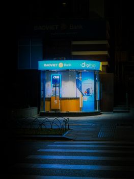 Illuminated ATM booth of BaoViet Bank at night on a Saigon street, vibrant colors.