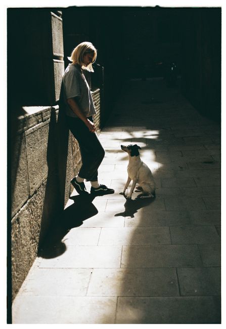 A woman stands in a sunlit alley with a sitting dog, creating a dramatic street scene.
