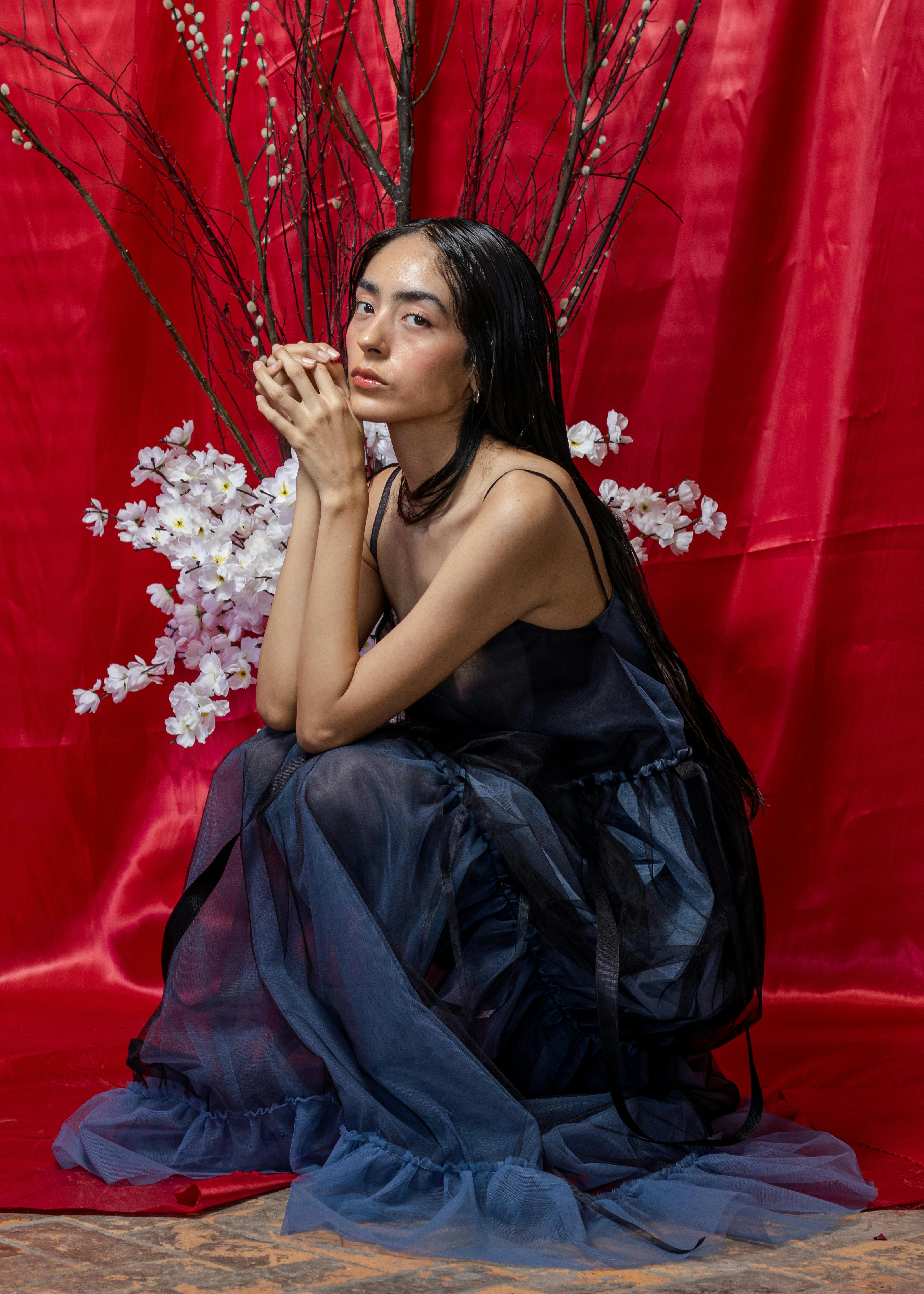 Artistic portrait of a woman seated elegantly with floral arrangement and red background.