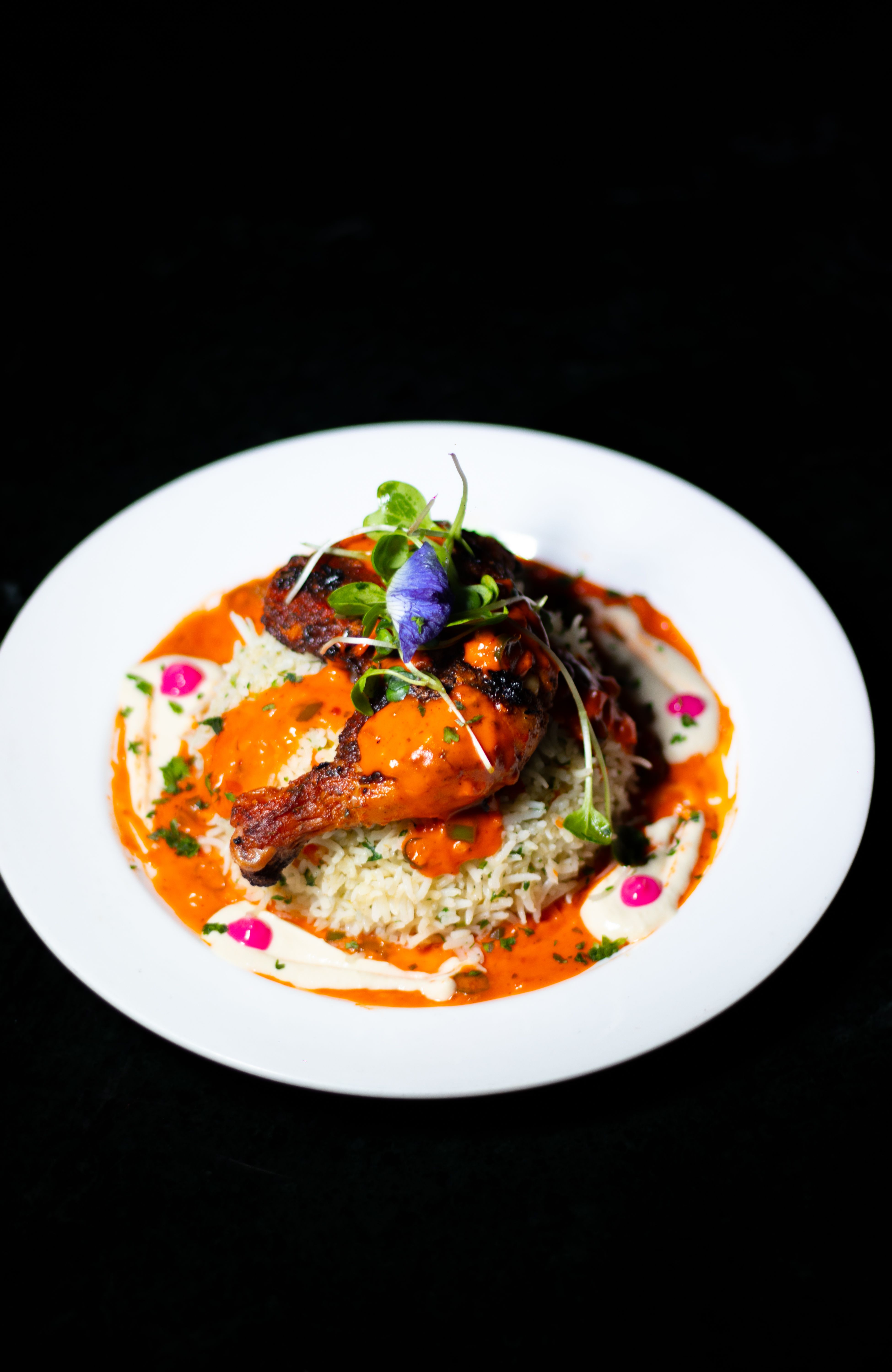 Elegant presentation of tandoori chicken with herb rice, creamy tomato sauce, and edible flowers.