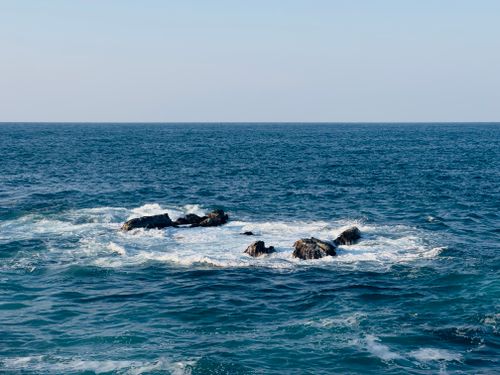Free A wide shot of waves crashing against rocks in the blue ocean during the day. Stock Photo