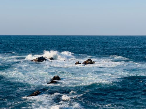 Free Vibrant ocean scene with waves crashing on rocks under clear blue sky. Stock Photo