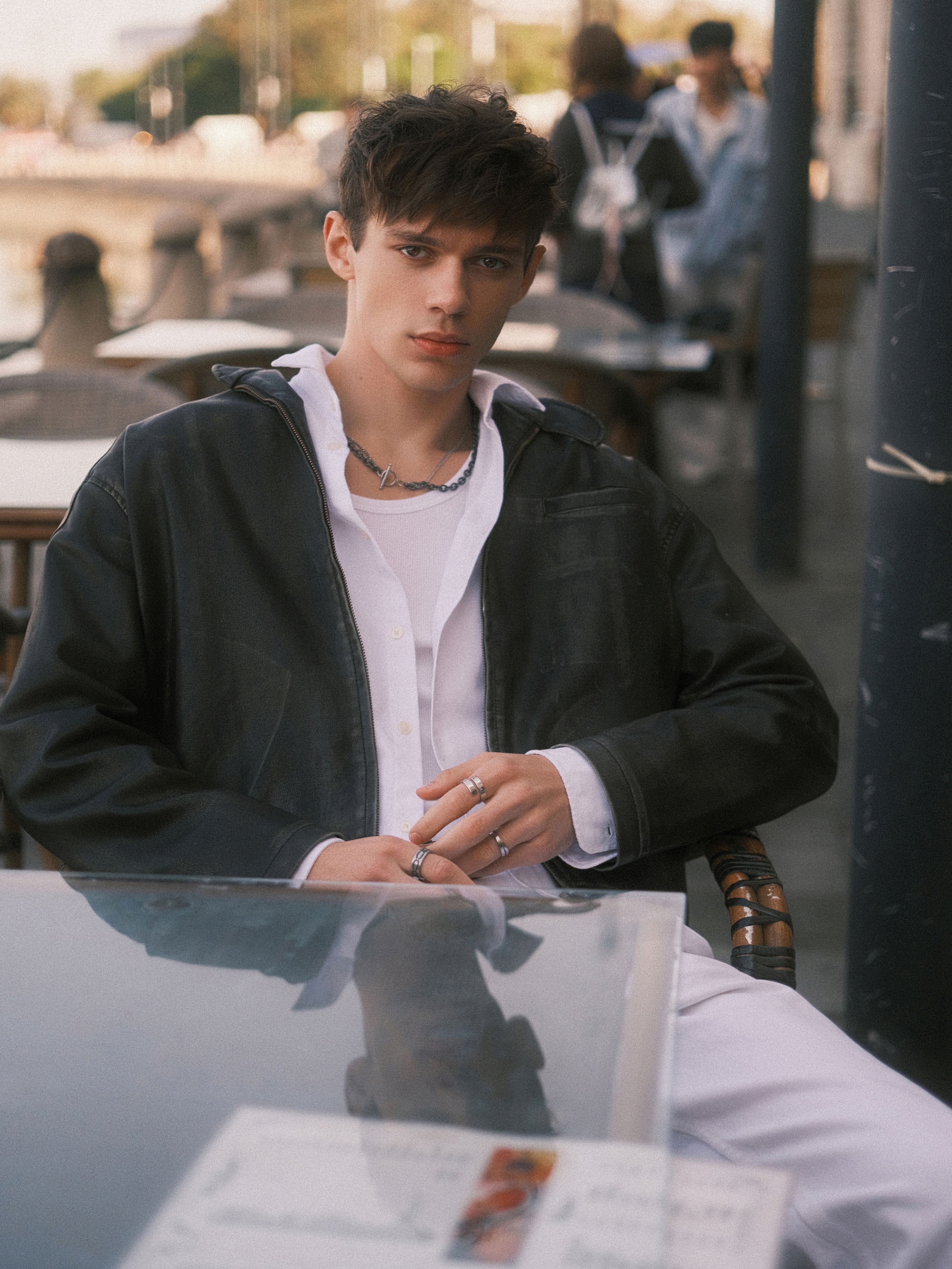 Stylish young man seated outdoors in a relaxed pose, exuding casual fashion.