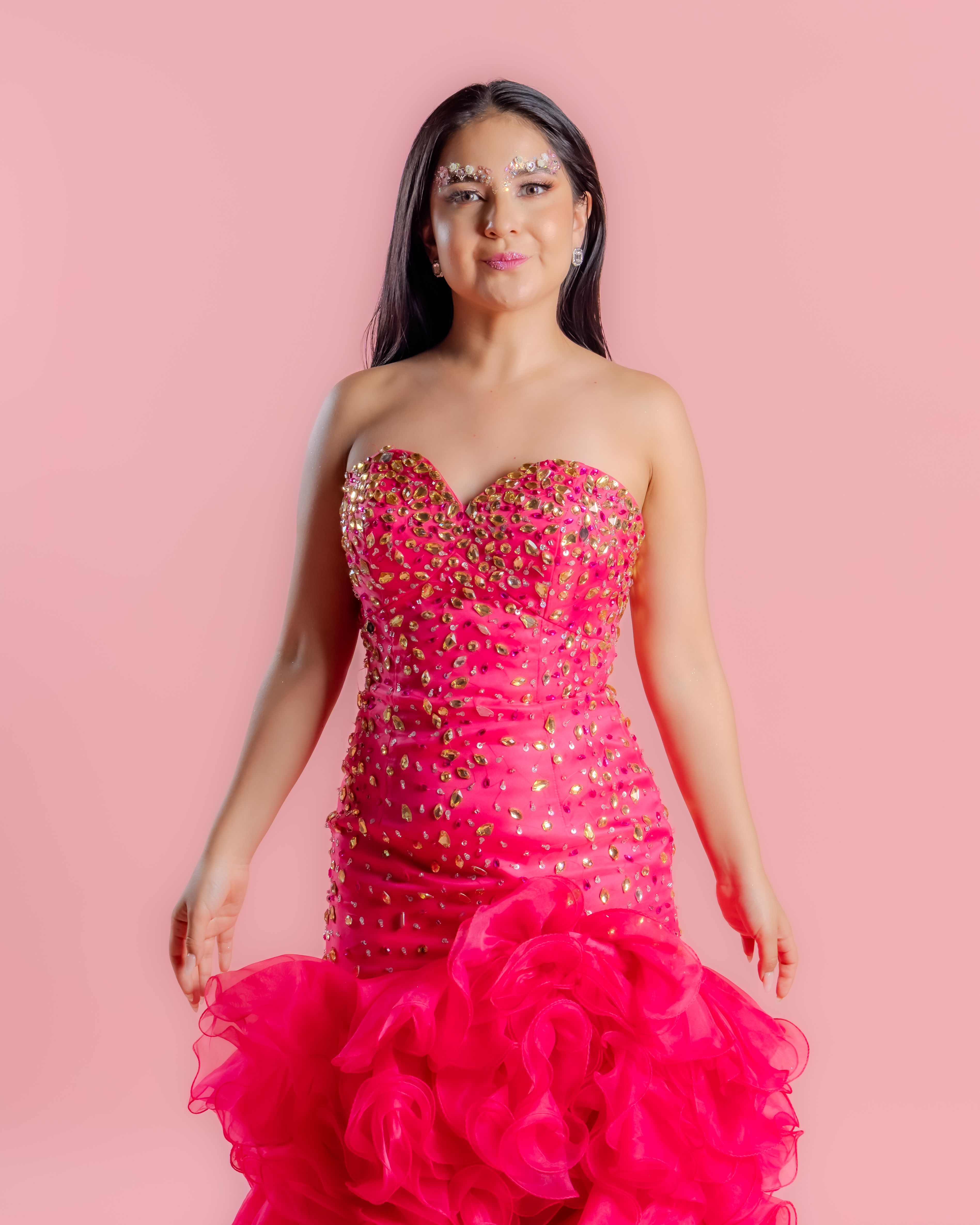 A woman in a stunning pink rhinestone gown stands confidently against a matching backdrop.