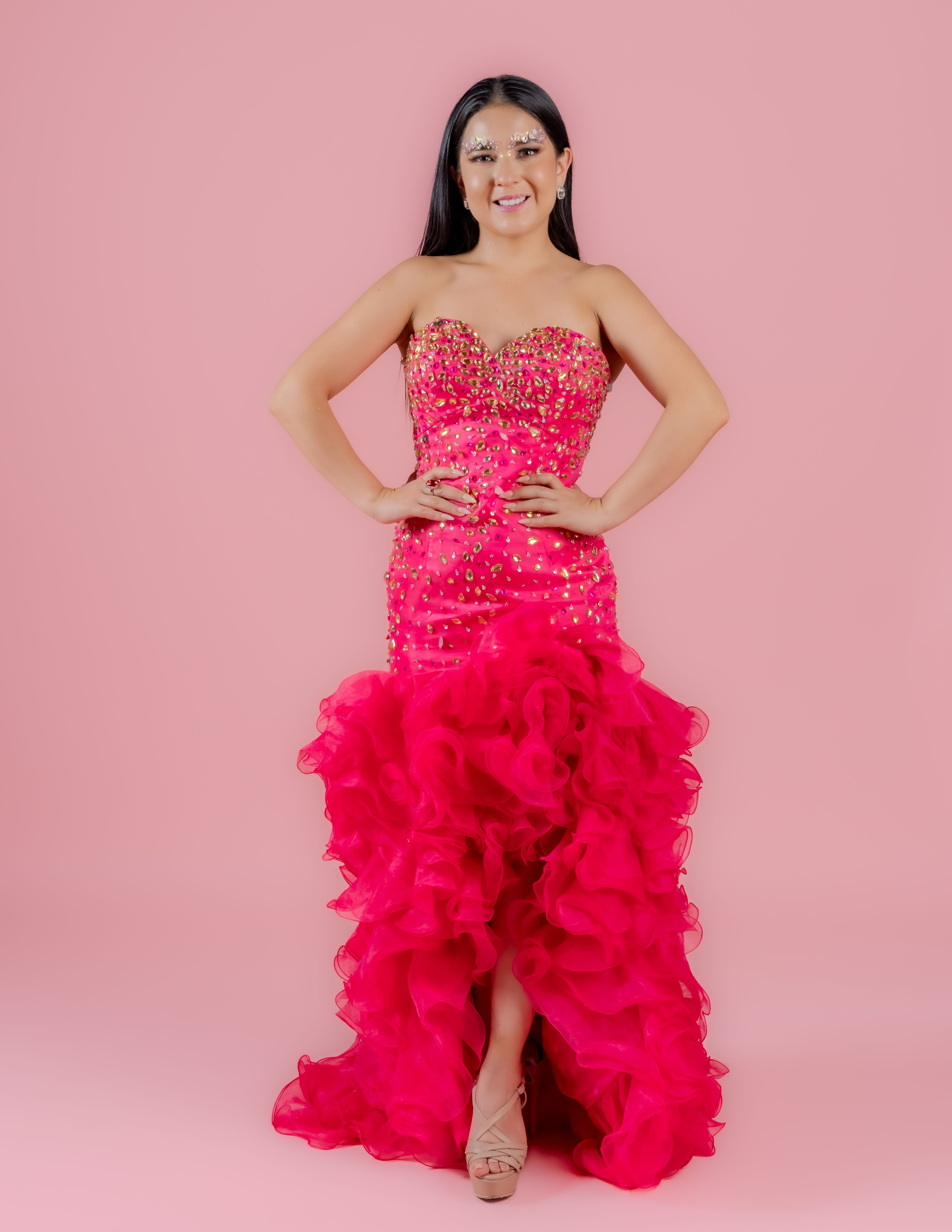 A woman poses gracefully in a glamorous pink dress with a ruffled skirt and jeweled bodice.