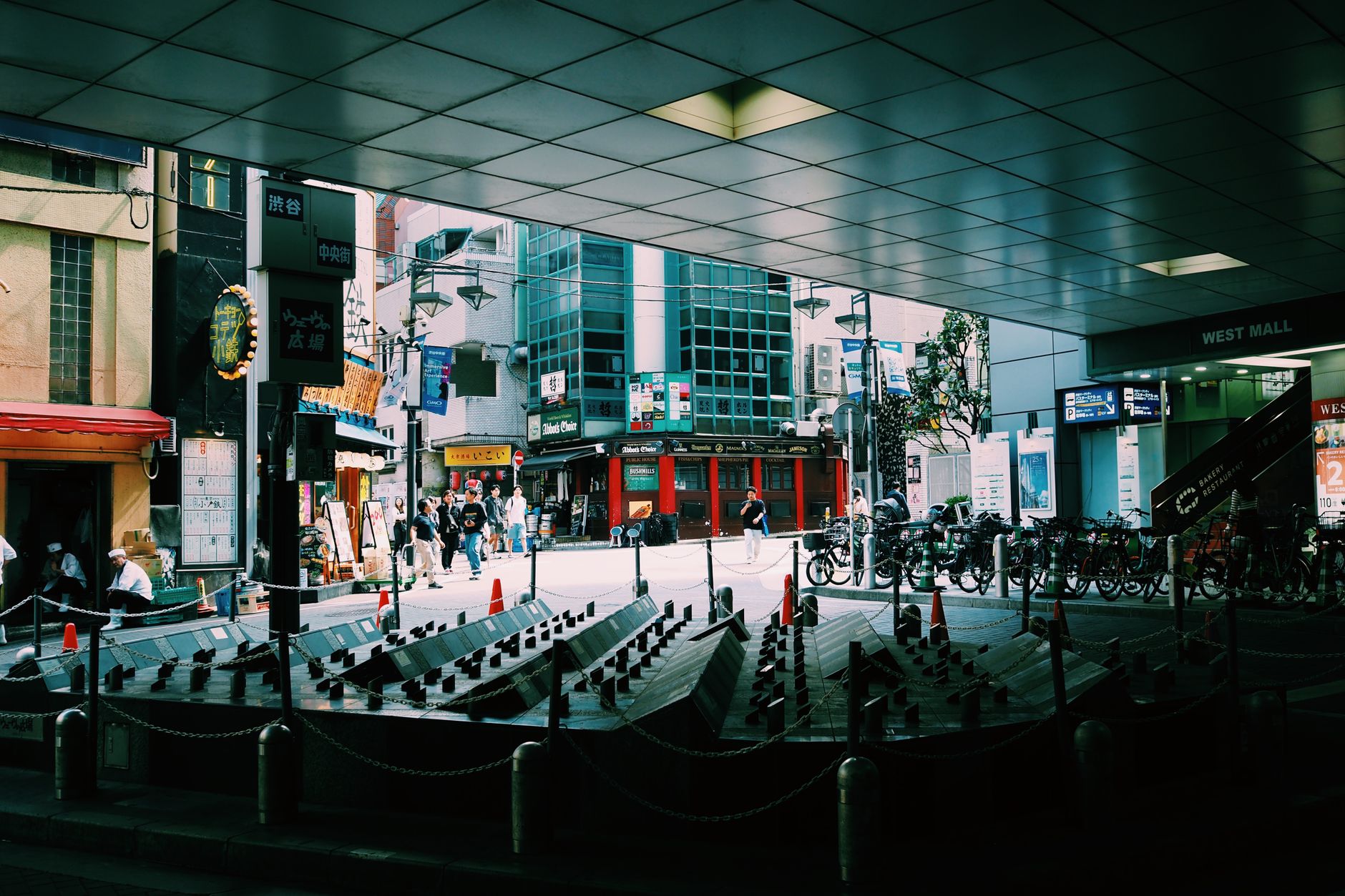 Busy Tokyo street with pedestrians, shops, and bicycles under an urban canopy.