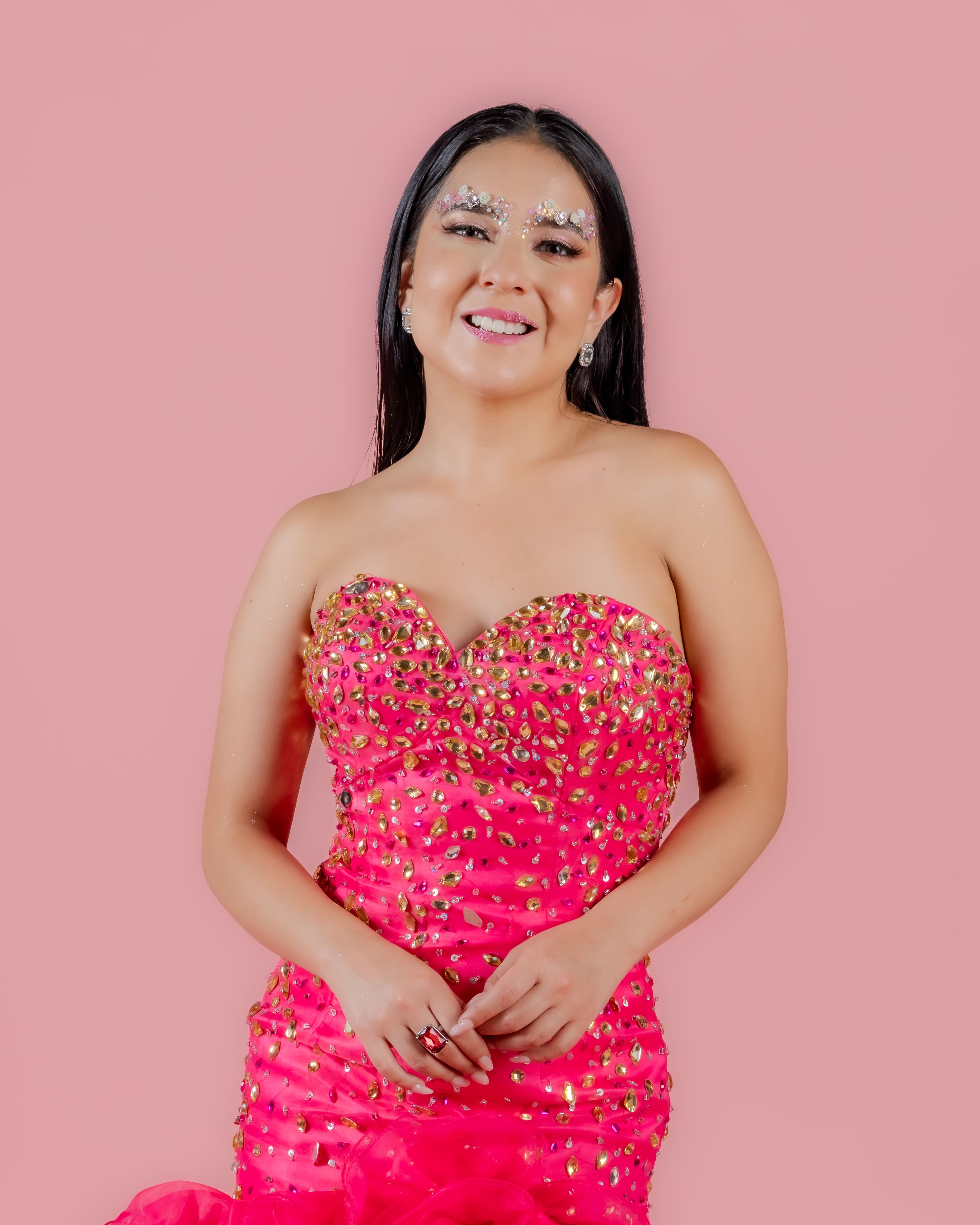 A graceful woman in a vibrant pink beaded gown radiates elegance against a soft background.