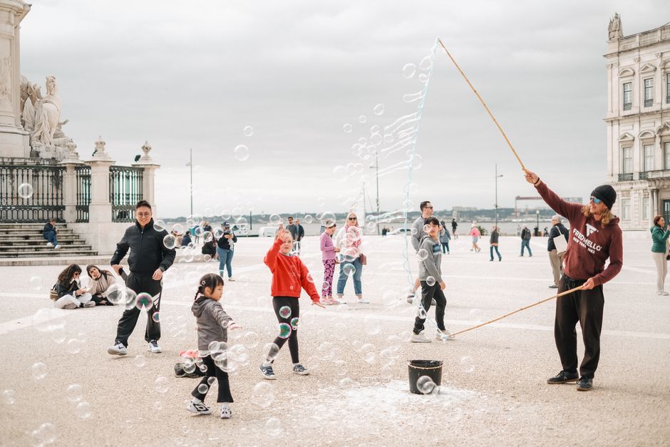 People enjoying bubble show by street performer in urban plaza setting.