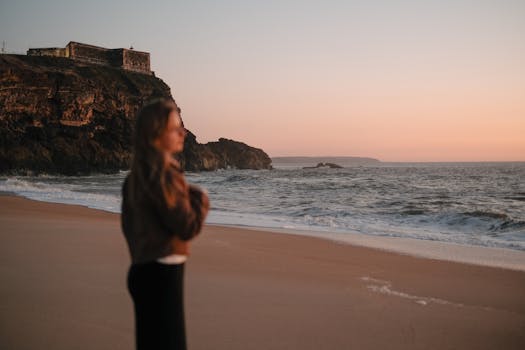 Silhouette of a woman gazing at a coastal sunset near the cliffs of Nazare, Portugal.