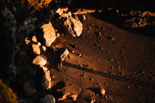 Free Footprints on a secluded sandy beach surrounded by large rocks, captured in warm, moody lighting. Stock Photo