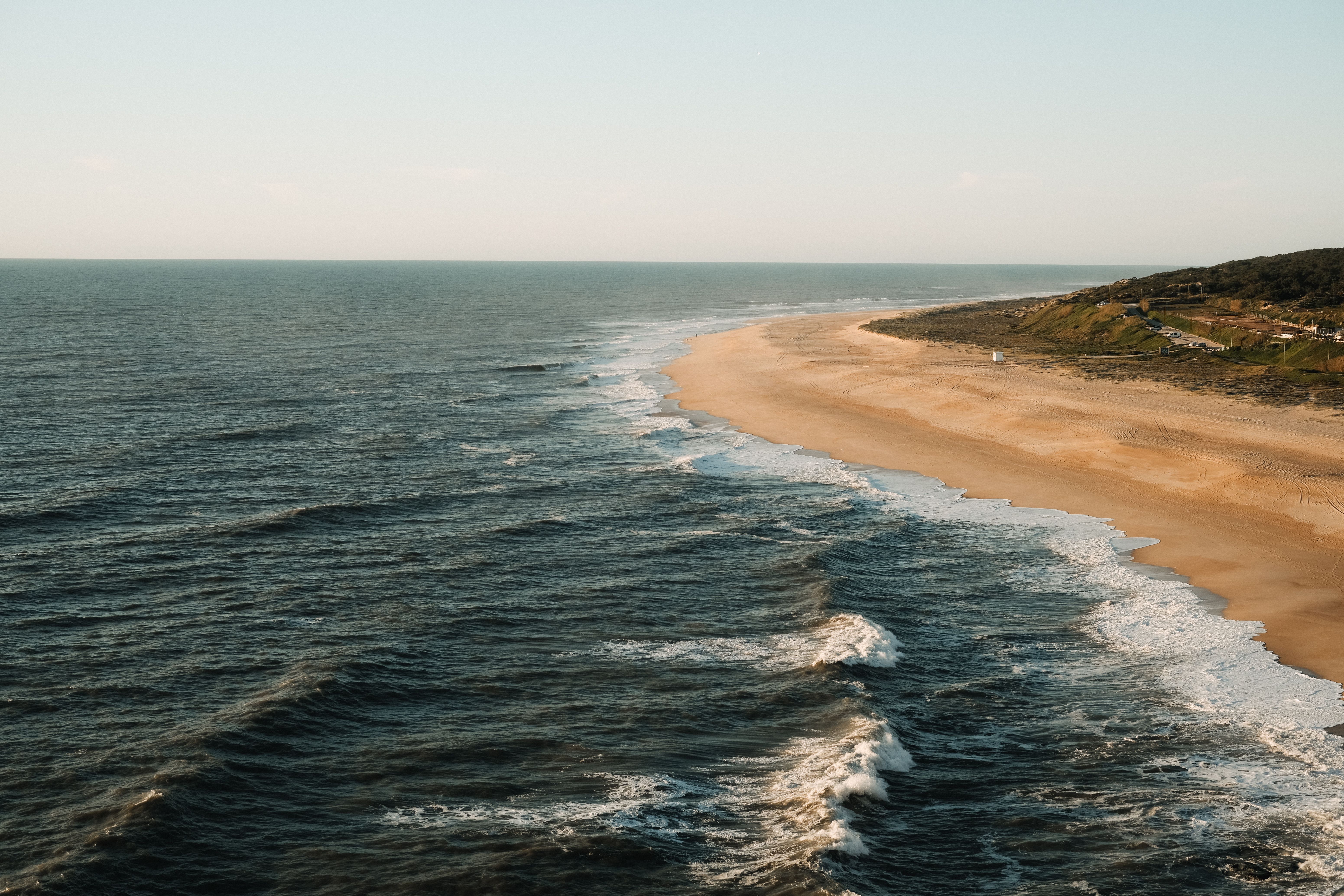 Aerial view of a tranquil beach and ocean waves on a sunny day, with golden sand and blue waters.