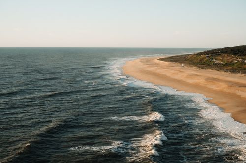 Free Aerial view of a tranquil beach and ocean waves on a sunny day, with golden sand and blue waters. Stock Photo