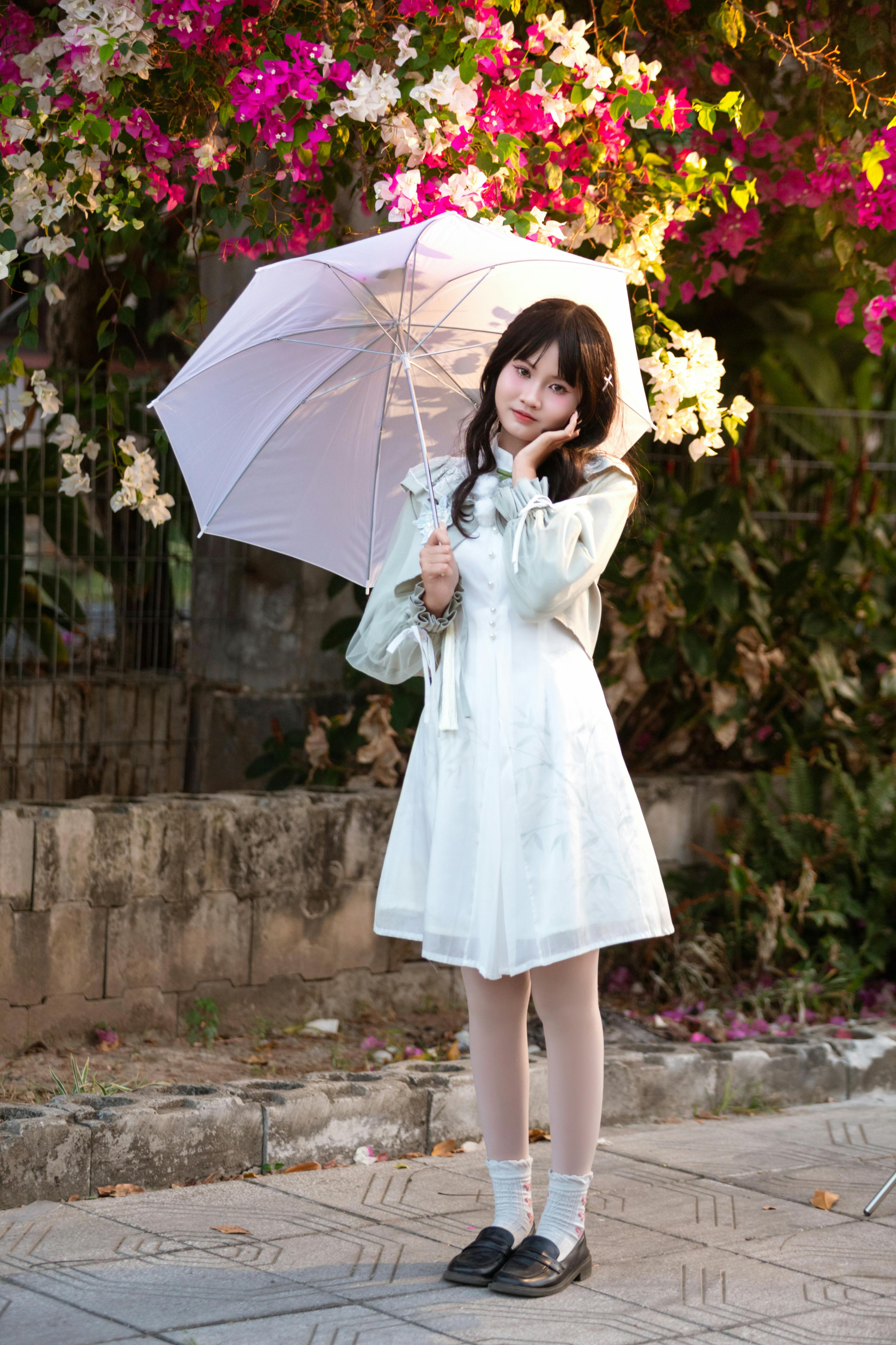 A young woman holding an umbrella, surrounded by colorful flowers outdoors.
