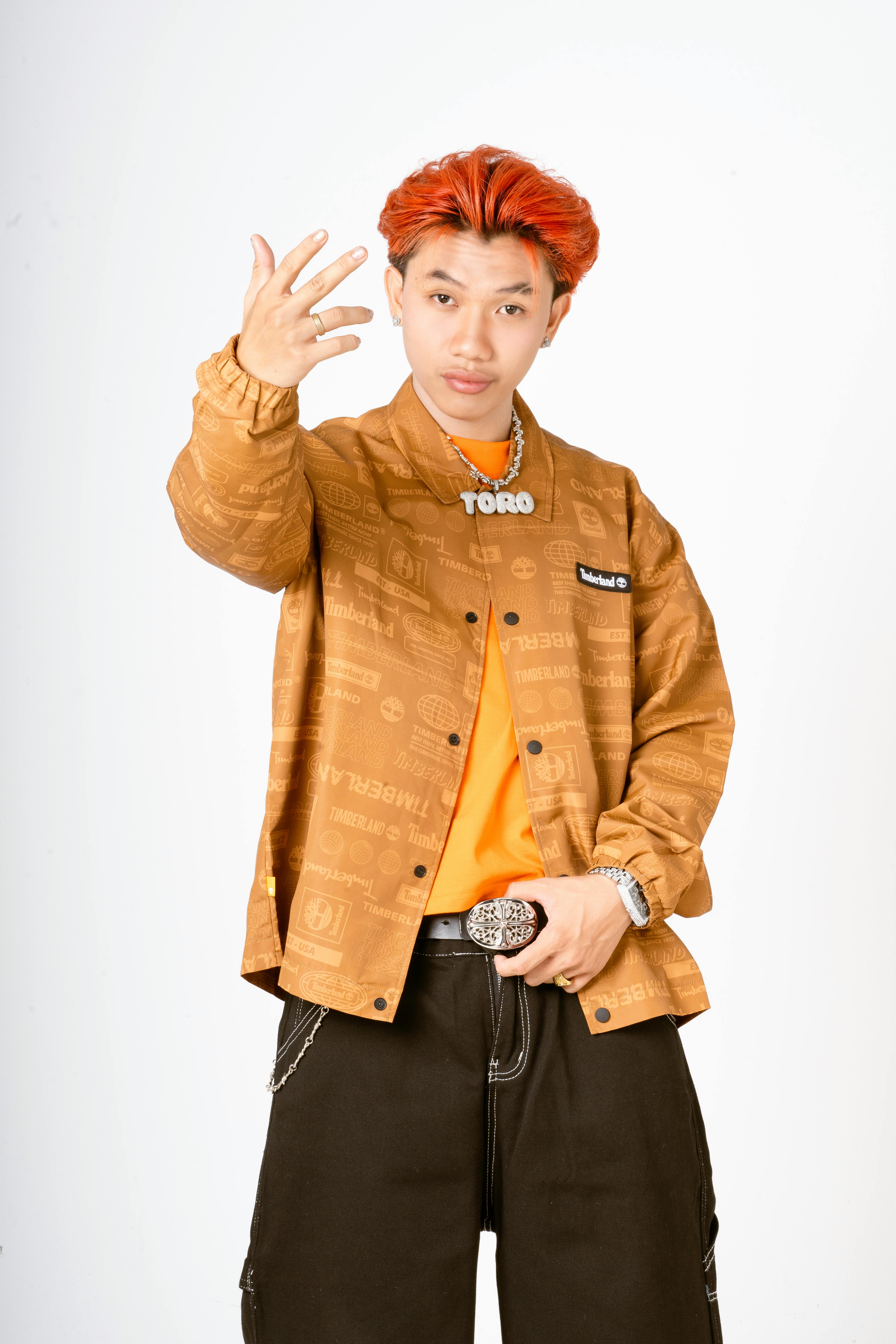 Portrait of a confident young man with red hair, wearing a stylish outfit, against a plain background.