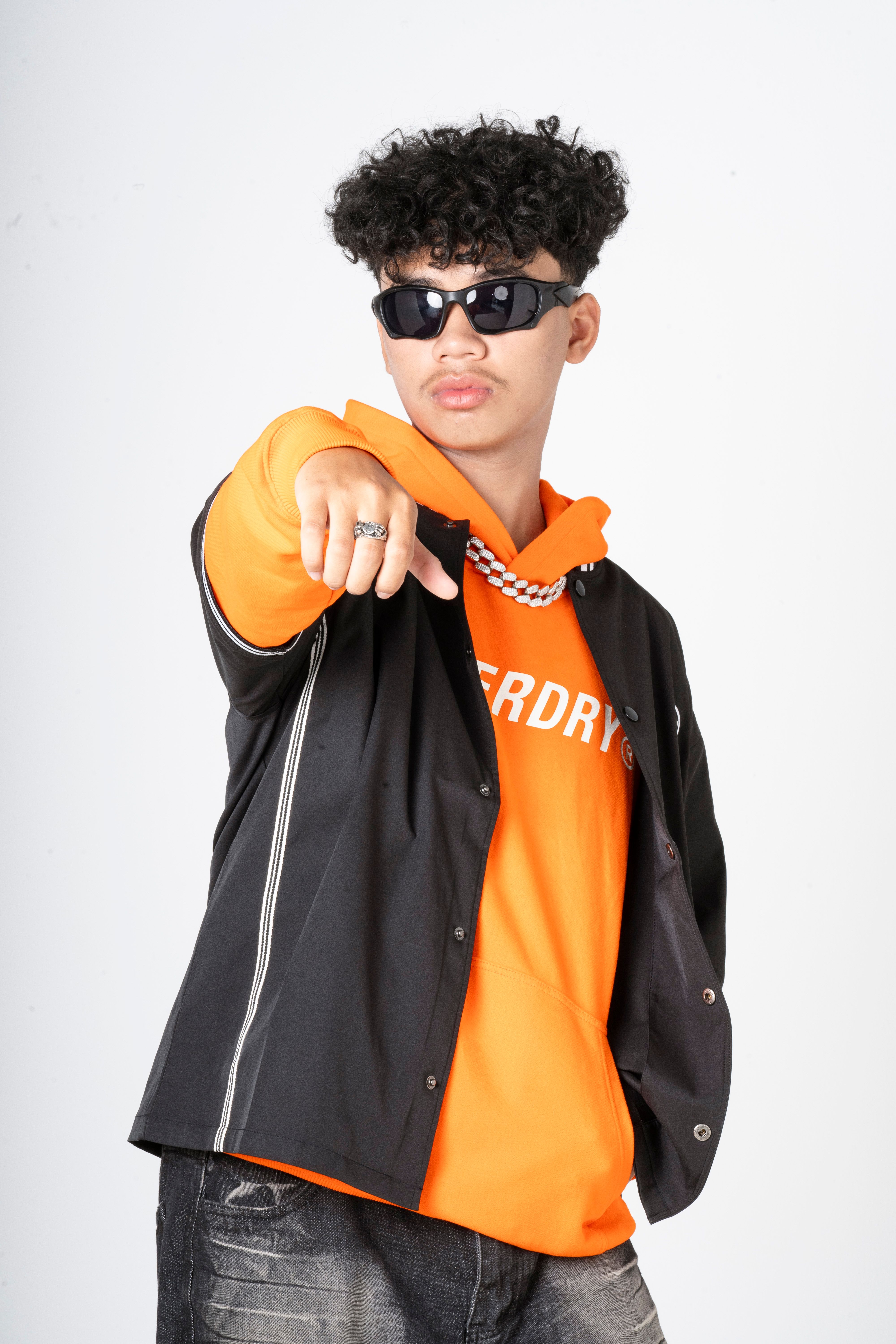 Young adult wearing trendy sunglasses and an orange hoodie, striking a confident pose against a plain background.